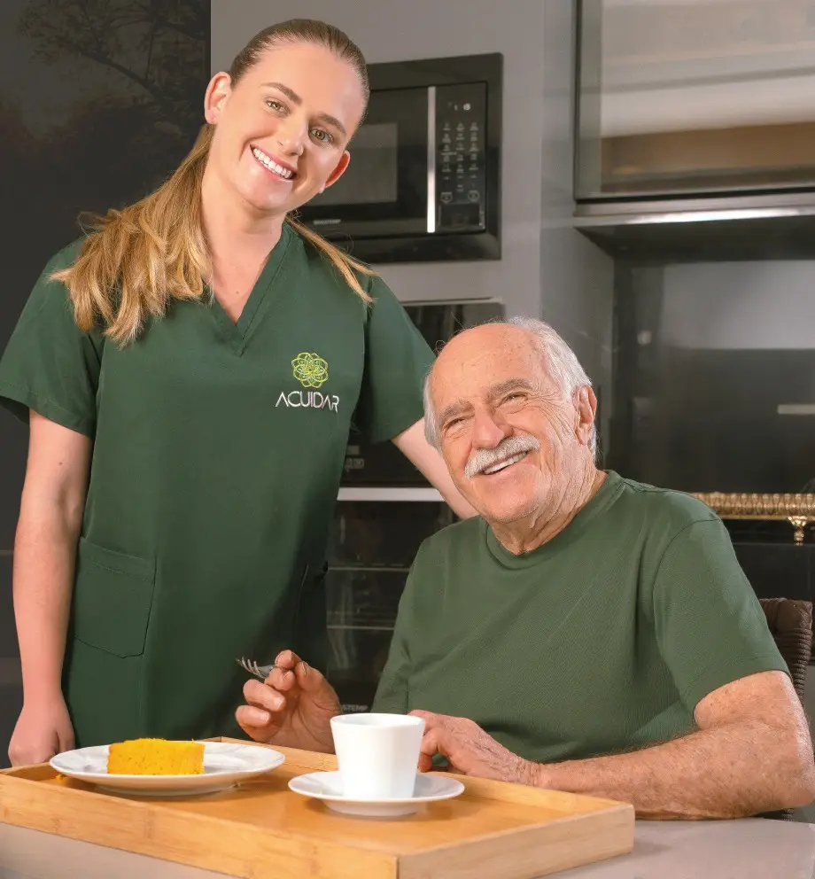 Cuidadora uniformizada sorrindo ao lado de senhora idosa